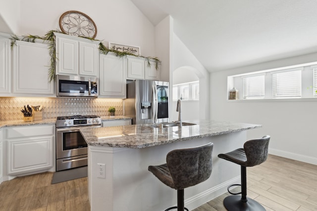 kitchen featuring light wood-type flooring, appliances with stainless steel finishes, a kitchen island with sink, and white cabinets