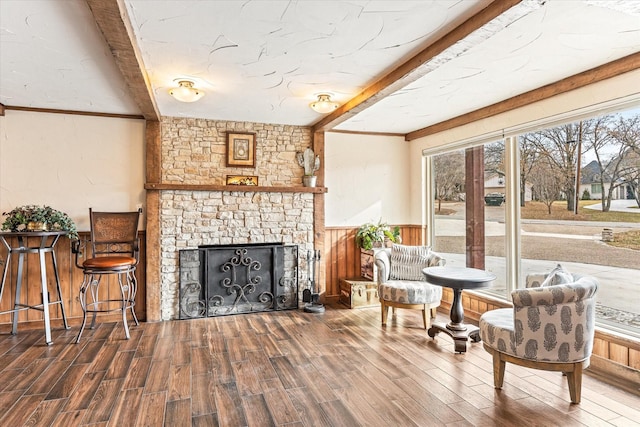 sitting room with beamed ceiling, hardwood / wood-style flooring, and a stone fireplace