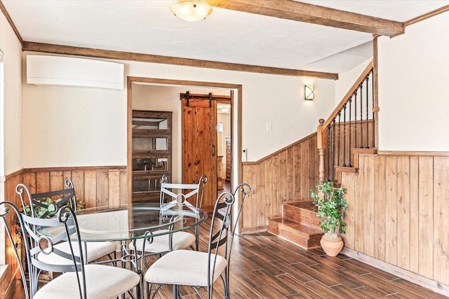 dining area with beam ceiling, dark wood-type flooring, a barn door, a wall unit AC, and wooden walls