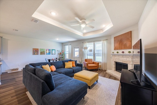 living area featuring ceiling fan, ornamental molding, a tray ceiling, dark wood finished floors, and a fireplace