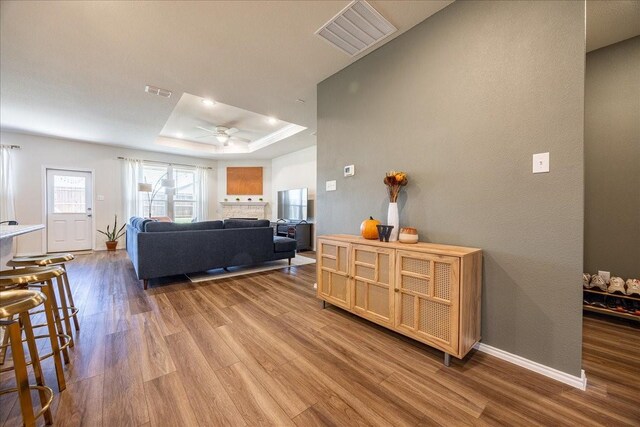 living room featuring a raised ceiling, dark wood-style flooring, a ceiling fan, and baseboards