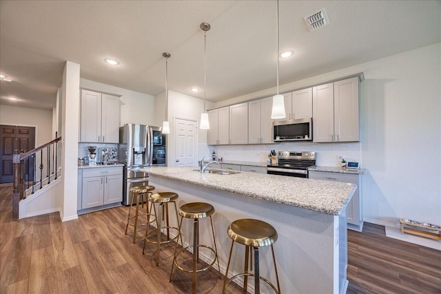 kitchen featuring stainless steel appliances, a sink, dark wood-style floors, a kitchen breakfast bar, and recessed lighting