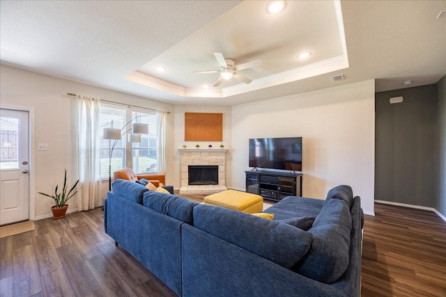 living room with a raised ceiling, baseboards, a stone fireplace, and dark wood-style flooring