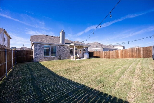 rear view of house featuring a fenced backyard, a lawn, a chimney, and brick siding