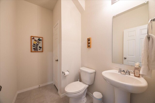 half bath with baseboards, a sink, and toilet