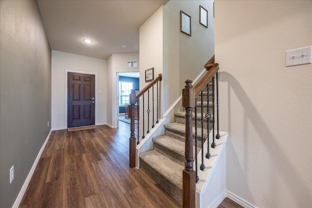 foyer entrance featuring dark wood finished floors, stairs, and baseboards