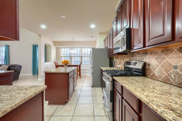 kitchen with light tile patterned flooring, appliances with stainless steel finishes, tasteful backsplash, light stone countertops, and decorative light fixtures