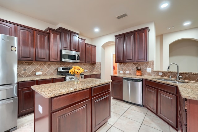 kitchen featuring light stone counters, a center island, sink, tasteful backsplash, and appliances with stainless steel finishes