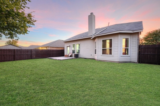 back house at dusk with a patio and a yard