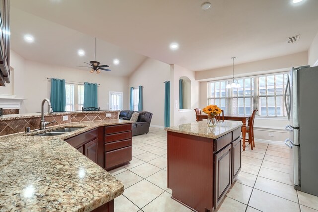 kitchen with vaulted ceiling, light tile patterned floors, sink, pendant lighting, and stainless steel fridge