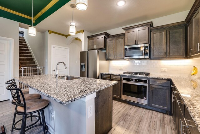 kitchen with light hardwood / wood-style floors, a center island with sink, sink, appliances with stainless steel finishes, and pendant lighting