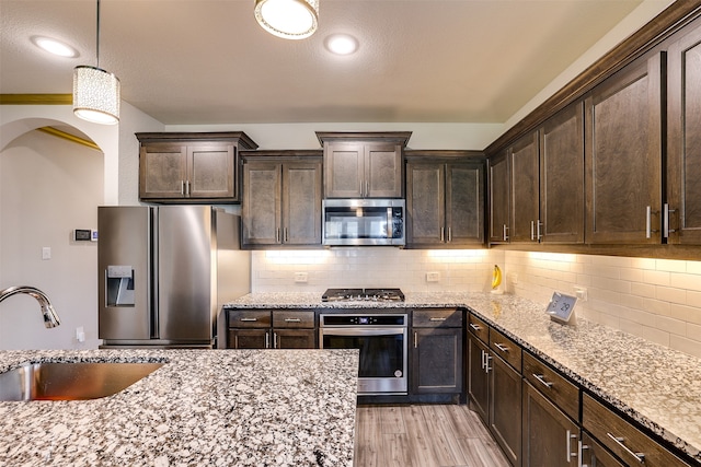 kitchen with dark brown cabinetry, stainless steel appliances, hanging light fixtures, and sink