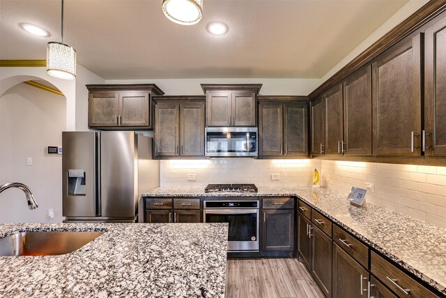 kitchen with dark brown cabinetry, stainless steel appliances, hanging light fixtures, and sink