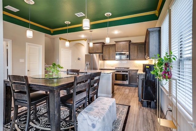 kitchen featuring stainless steel appliances, light hardwood / wood-style floors, dark brown cabinetry, ornamental molding, and pendant lighting