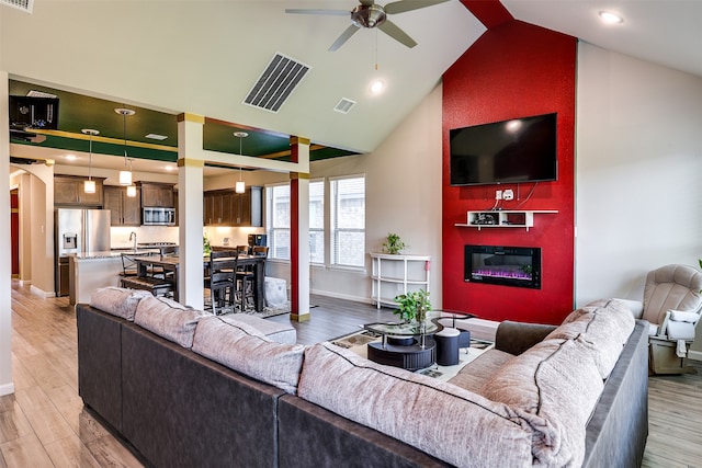 living room featuring light wood-type flooring, ceiling fan, sink, and high vaulted ceiling