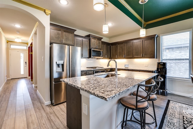 kitchen with light stone counters, crown molding, stainless steel appliances, decorative light fixtures, and sink