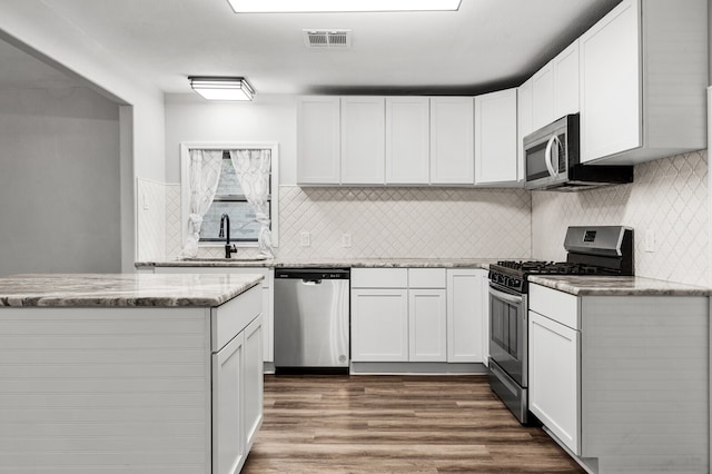 kitchen with dark wood-type flooring, white cabinetry, light stone countertops, and stainless steel appliances