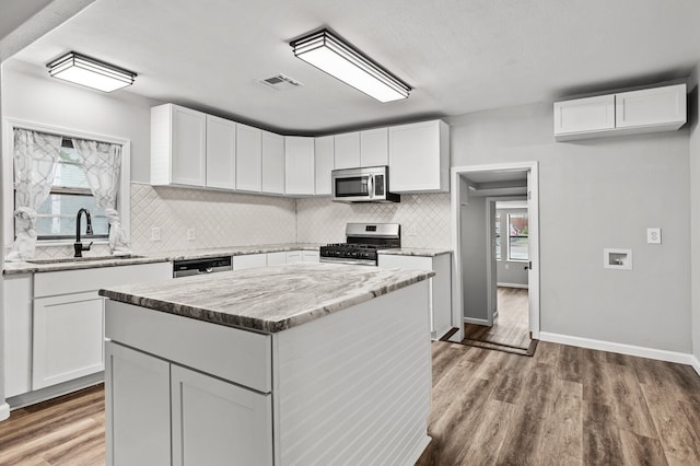 kitchen with light hardwood / wood-style floors, sink, a kitchen island, white cabinetry, and appliances with stainless steel finishes