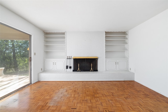 unfurnished living room featuring a fireplace, built in features, and light parquet floors