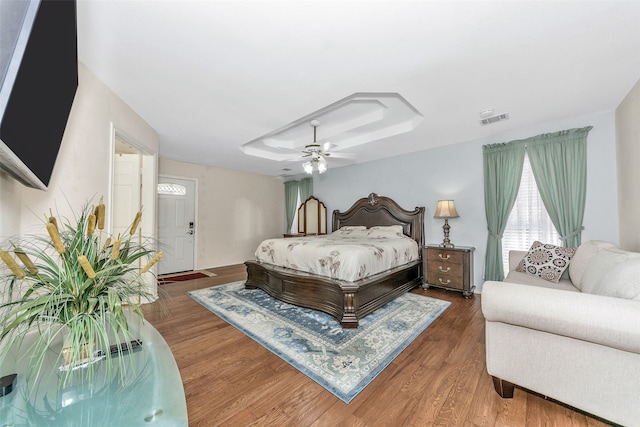 bedroom with a raised ceiling, ceiling fan, and dark hardwood / wood-style floors