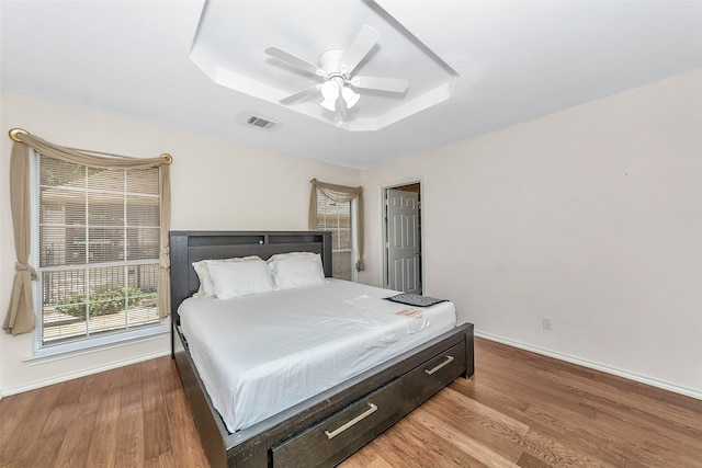 bedroom featuring a tray ceiling, wood-type flooring, and ceiling fan