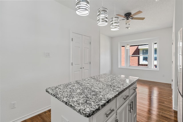 kitchen featuring light stone counters, white cabinetry, dark hardwood / wood-style floors, ceiling fan, and a center island