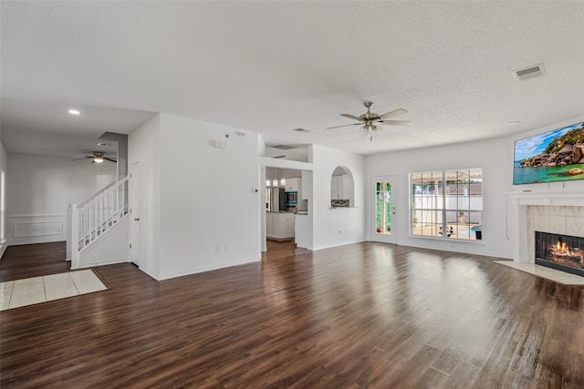 unfurnished living room featuring a textured ceiling, a tiled fireplace, dark wood-type flooring, and ceiling fan