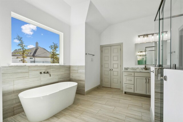 bathroom featuring tile walls, a tub to relax in, vanity, and lofted ceiling