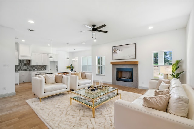 living room with ceiling fan with notable chandelier and light hardwood / wood-style floors