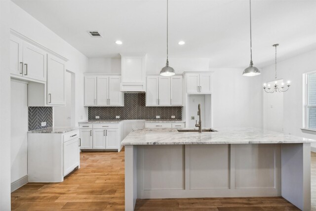 kitchen featuring a center island with sink, white cabinetry, hanging light fixtures, sink, and light hardwood / wood-style flooring