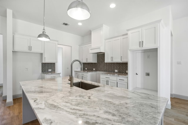 kitchen with white cabinetry, sink, hardwood / wood-style floors, a kitchen island with sink, and pendant lighting