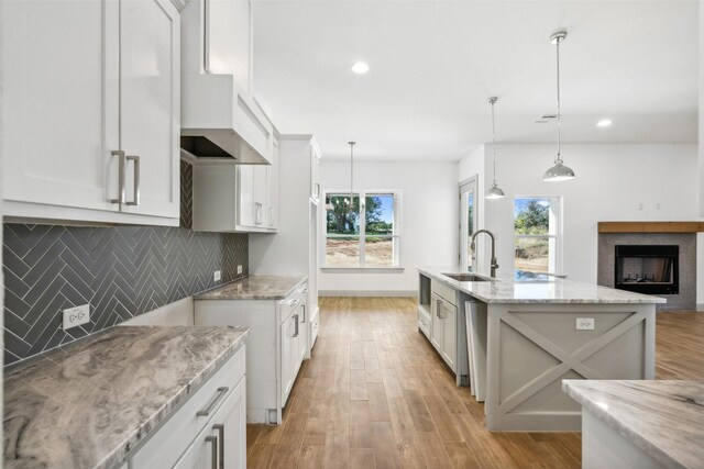 kitchen featuring white cabinets, sink, an island with sink, light wood-type flooring, and decorative light fixtures