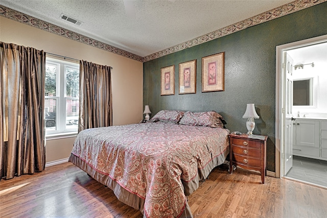 bedroom with ensuite bathroom, wood-type flooring, and a textured ceiling