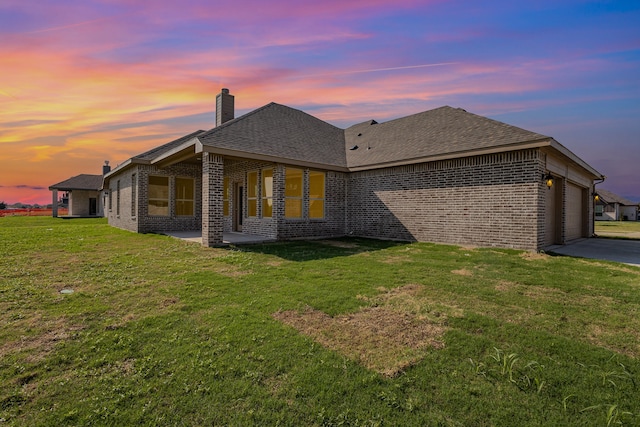 back house at dusk with a garage and a yard