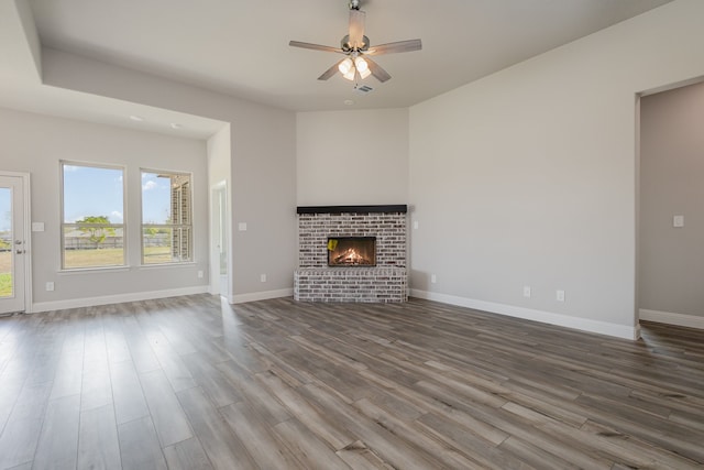 unfurnished living room featuring a brick fireplace, hardwood / wood-style flooring, and ceiling fan