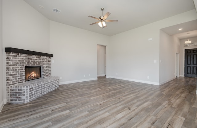 unfurnished living room with a brick fireplace, wood-type flooring, and ceiling fan