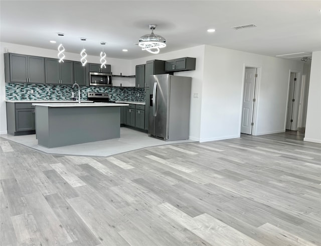 kitchen featuring gray cabinetry, a center island with sink, and stainless steel appliances