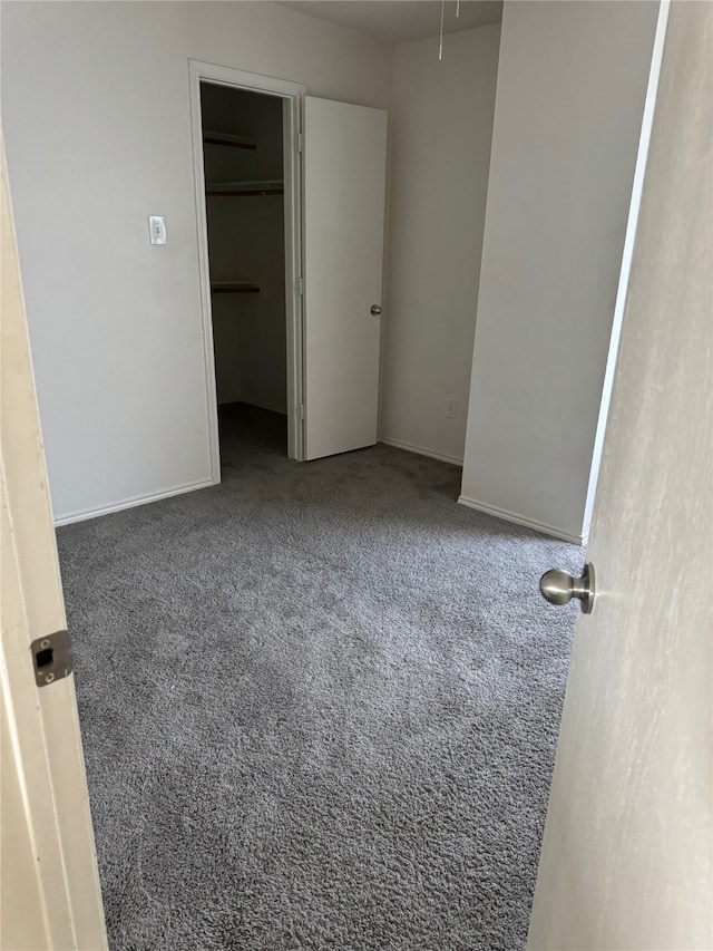 unfurnished bedroom with dark carpet, a spacious closet, and a closet