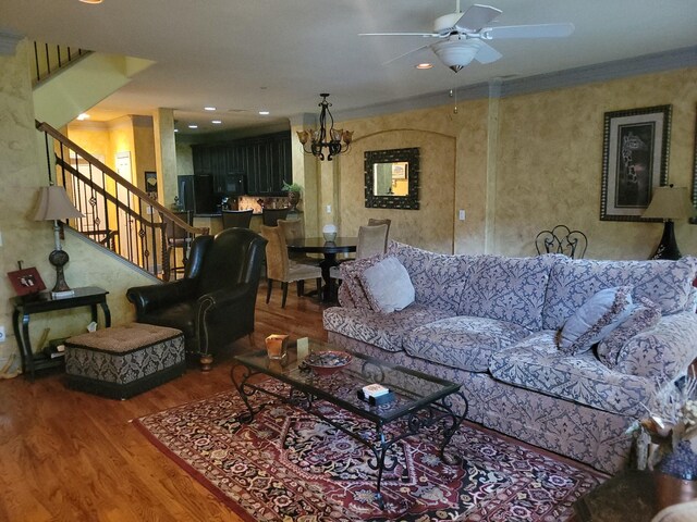 living room featuring wood-type flooring, ceiling fan with notable chandelier, and crown molding