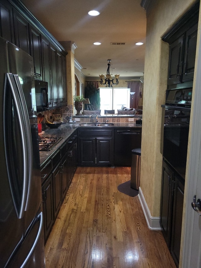 kitchen featuring dark wood-type flooring, sink, an inviting chandelier, kitchen peninsula, and black appliances