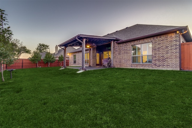 back house at dusk featuring a yard and a patio