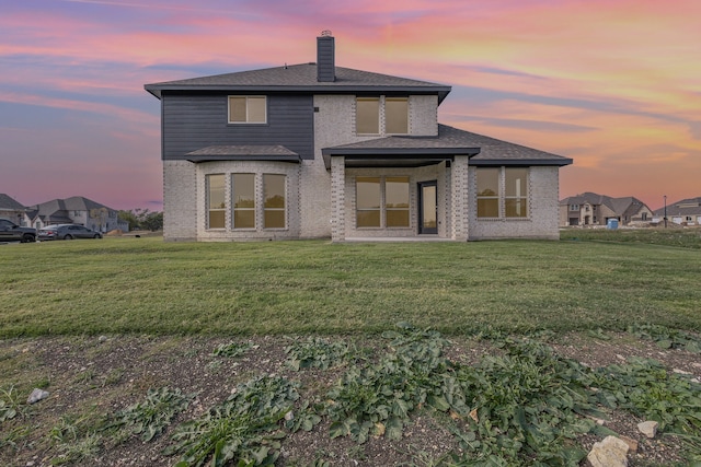 back house at dusk featuring a lawn