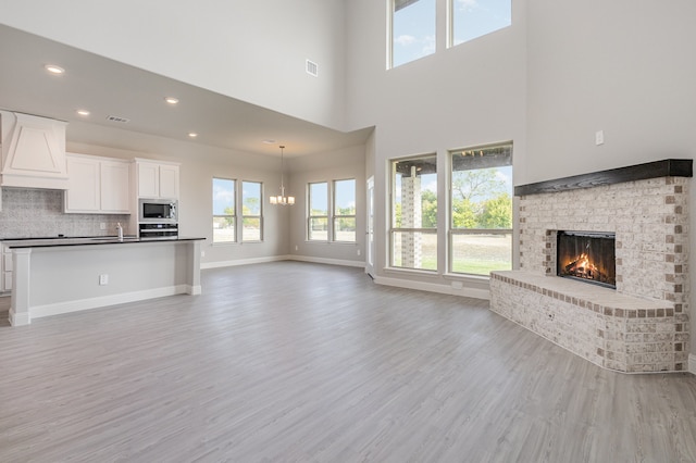 unfurnished living room featuring a brick fireplace, light wood-type flooring, a notable chandelier, and a towering ceiling