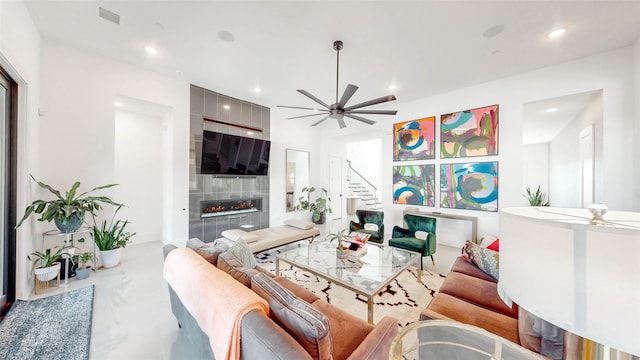 living room with a tile fireplace and ceiling fan