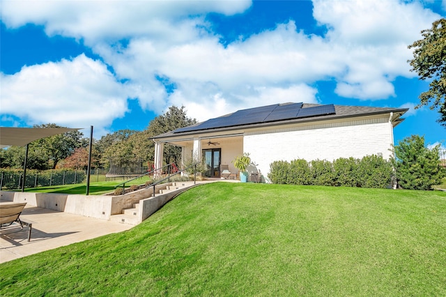 rear view of house featuring ceiling fan, a yard, a patio, and solar panels