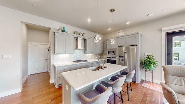 kitchen featuring appliances with stainless steel finishes, decorative light fixtures, light hardwood / wood-style floors, and wall chimney range hood