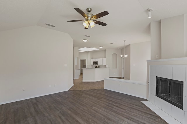 unfurnished living room featuring ceiling fan with notable chandelier, dark hardwood / wood-style flooring, lofted ceiling, and a tile fireplace