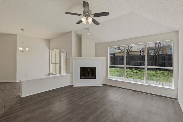 unfurnished living room featuring ceiling fan with notable chandelier, a textured ceiling, dark wood-type flooring, a tile fireplace, and vaulted ceiling