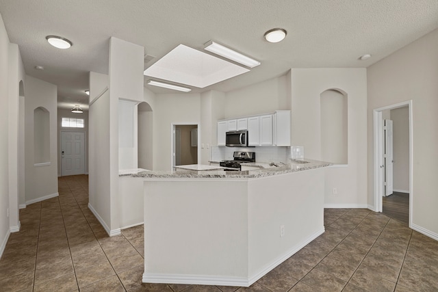 kitchen featuring stainless steel appliances, white cabinetry, kitchen peninsula, light stone countertops, and a textured ceiling