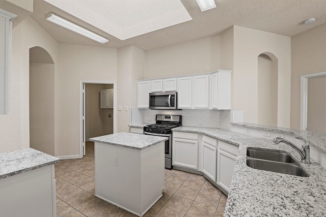 kitchen with white cabinets, sink, a kitchen island, light stone countertops, and appliances with stainless steel finishes